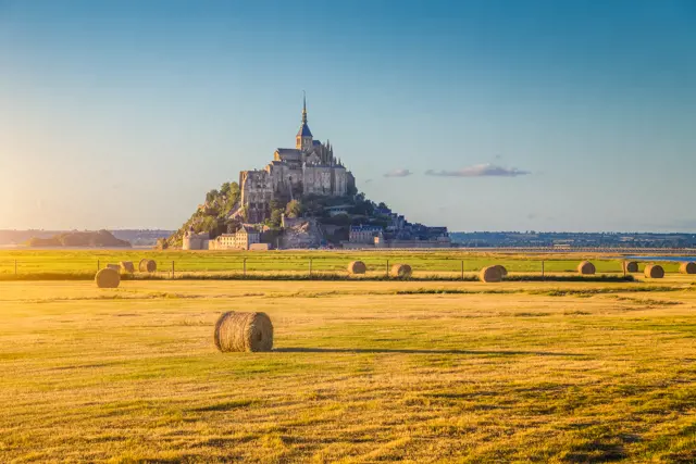beautiful view of famous historic le mont saint michel tidal island in beautiful golden evening light at sunset in summer with hay bales on empty fields normandy northern france