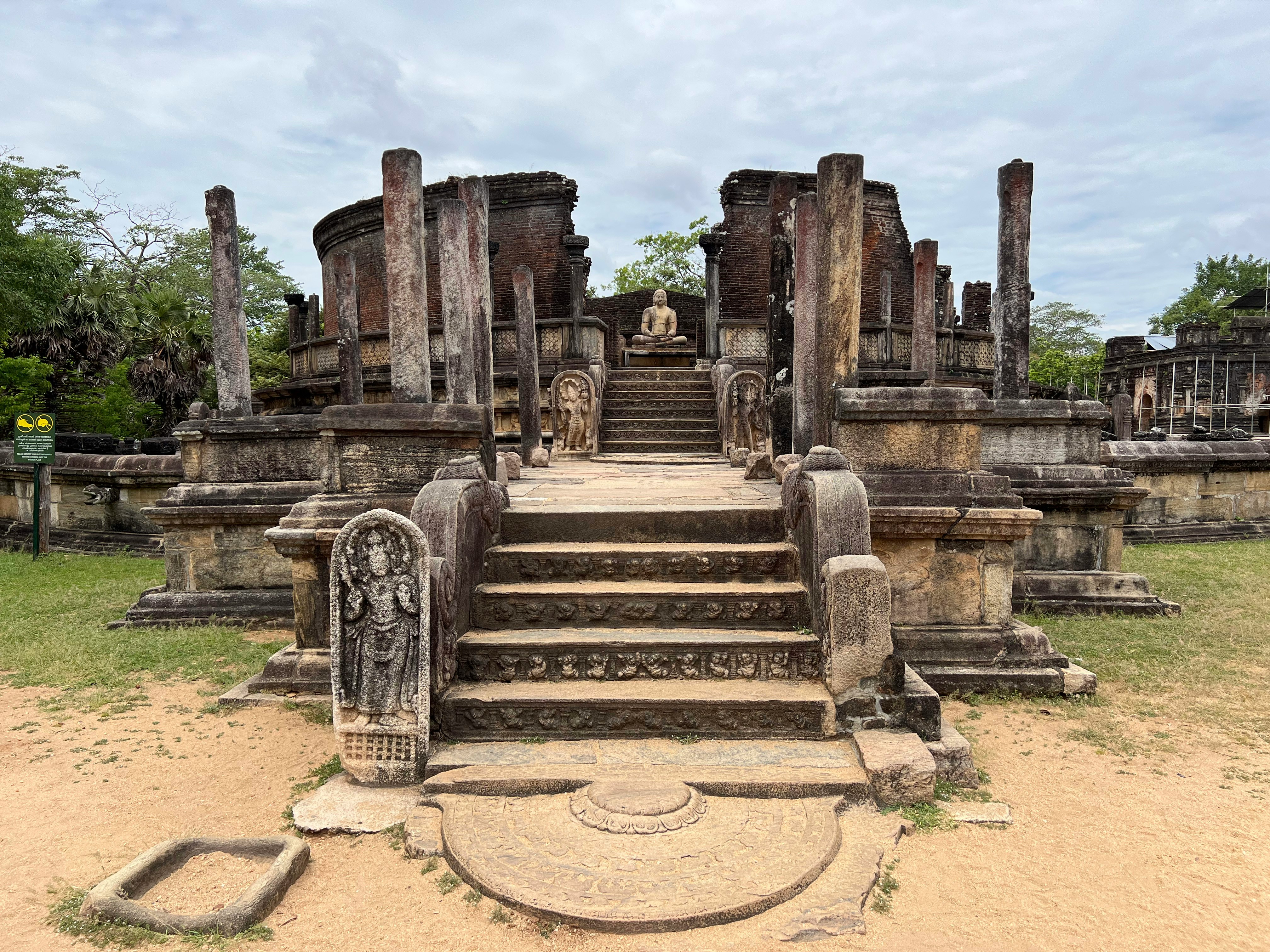 ancient ruins featuring a grand stone staircase leading to a raised platform with a seated buddha statue
